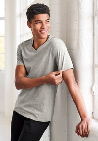 Graues V-Ausschnitt-T-Shirt aus weichem, leichtem Stoff, mit kurzen Ärmeln und einer lockeren Passform, kombiniert mit schwarzen Hosen.
