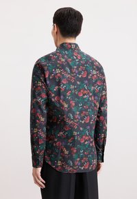 Camicia a maniche lunghe floreale con sfondo scuro. Caratterizzata da fiori e foglie multicolori in rosso, verde, viola e giallo. Tessuto morbido.