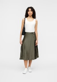 Πράσινη φούστα με σχέδιο πουά, σε συνδυασμό με άσπρο τοπάκι και μαύρη τσάντα ώμου. Το μοντέλο φορά λευκά αθλητικά παπούτσια.