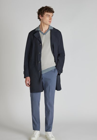 Granatowy płaszcz trench z zapięciem na guziki, jasnoszary sweter z dzianiny oraz jasnoniebieskie dopasowane spodnie. Całość dopełniają białe trampki.