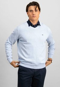 Világoskék kevert pamut pulóver, V nyakkivágással, bordás mandzsettákkal és szegéllyel, sötét színű, galléros inggel alatta.