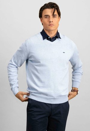 Hellblauer Pullover aus Baumwollmischung, mit V-Ausschnitt, gerippten Bündchen und Saum, kombiniert mit einem dunklen Hemd mit Kragen darunter.