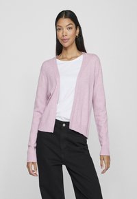 Cardigan rosa con orlo e polsini a coste, design aperto, indossato sopra una maglietta bianca e pantaloni neri. Tessuto morbido, vestibilità casual.