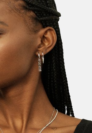 Silver earrings featuring the word "DREAM" in a bold font, with a pointed accent below. The design is sleek and modern.