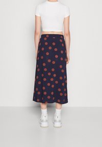 Falda de marina con grandes lunares de color óxido, hasta los tobillos, con cinturilla elástica, combinada con zapatillas blancas y calcetas hasta el tobillo.