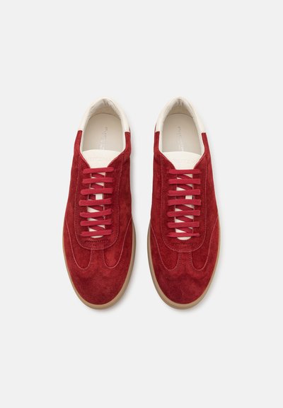 Baskets en suede rouge avec un col en crème lisse et des lacets rouges. Elles présentent un design épuré et une semelle en caoutchouc beige clair.