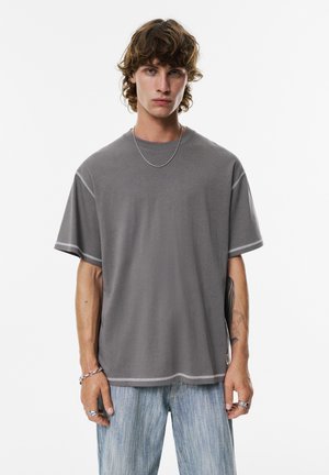 Gray short-sleeve T-shirt with a round neckline, contrasting stitching, and a relaxed fit, paired with light blue distressed jeans.
