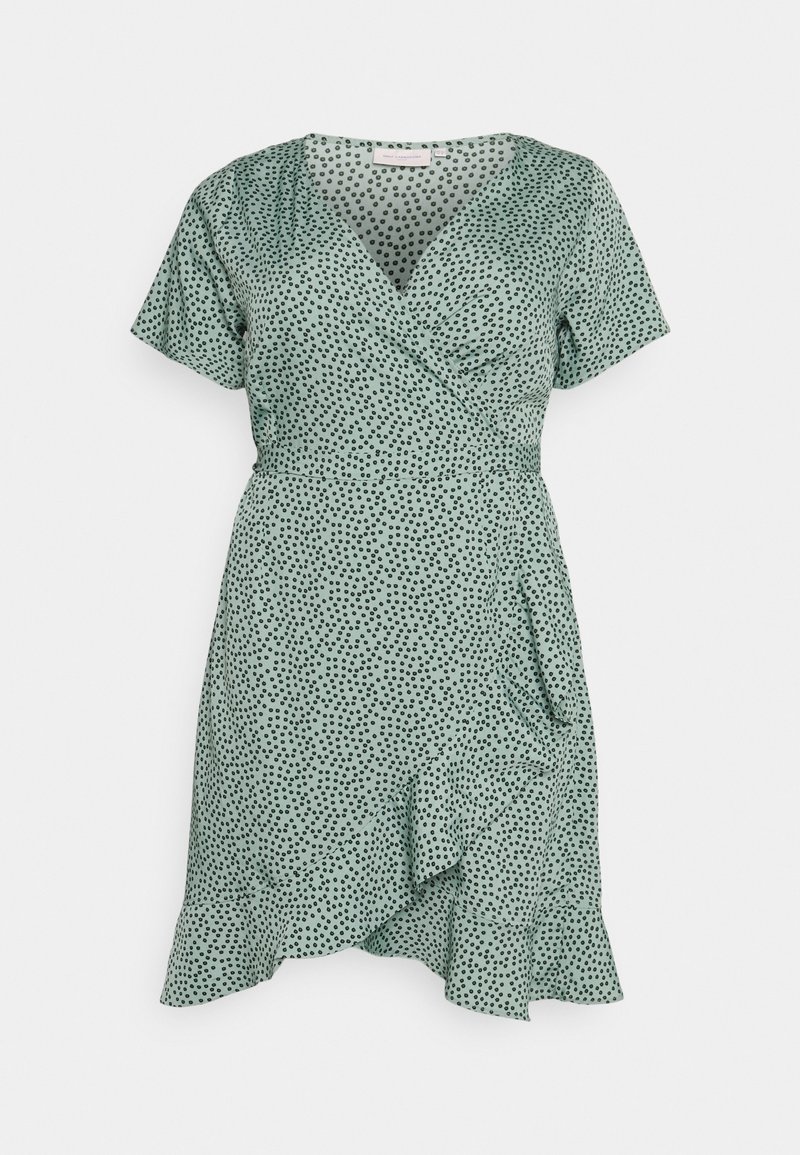 Robe verte à pois avec des manches courtes, design enroulé, ourlet à volants et texture de tissu doux. Présente de petits pois noirs sur un fond pastel.
