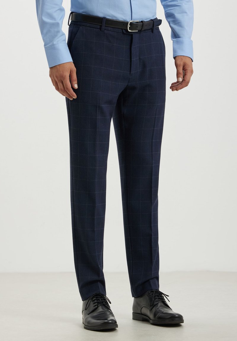Pantalons en tissu à carreaux navy avec une coupe slim, fabriqués à partir d'un tissu texturé. Associés à des chaussures noires et une ceinture noire pour un look soigné.