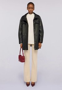Czarny skórzany płaszcz zapinany na zatrzaski, z dwoma kieszeniami na piersi. Do tego kremowa bluzka i beżowe rozszerzane spodnie. Czerwona torebka, bordo szpilki.