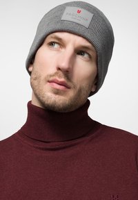 Szary dzianinowy beret z metką z logo "PROCHNIK", noszony z bordowym swetrem typu golf. Skoncentrowano się na ribbowanym wzorze i dopasowanym kroju.