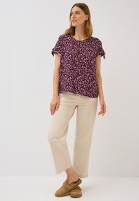 Haut à manches courtes bordeaux avec des motifs de feuilles blanches, présentant des manches nouées. Assorti à un pantalon large beige clair et des chaussures marron à enfiler.