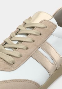 Αθλητικό παπούτσι σε μπεζ και ανοιχτό μπλε χρώμα με σουέντ και γυαλιστερές μεταλλικές λεπτομέρειες, κορδόνια με υφή και σχεδιασμό με στρώσεις ρίγες.