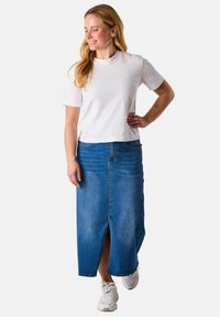 Denim maxi skirt in medium blue with a front slit, paired with a plain white short-sleeve t-shirt. Model wears white sneakers.