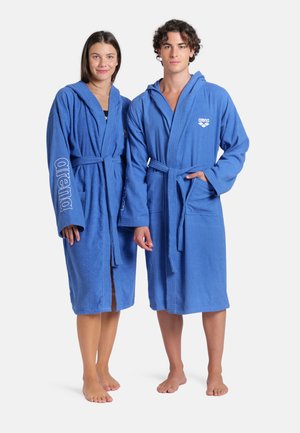 Batas de baño azules de rizo con mangas largas, cinturones en la cintura y un logo en la parte delantera. Ambas batas tienen bolsillos frontales.