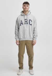Sweat à capuche gris avec motif "ARC" bleu marine, doté d'une capuche avec cordon de serrage ; associé à un pantalon kaki et des baskets blanches. Design simple et décontracté.
