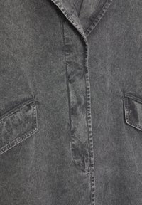 Harmaa farkkutakki, jossa on kaulus, etupainonappi ja kaksi rintataskua. Kangas on pehmeä ja teksturoitu.