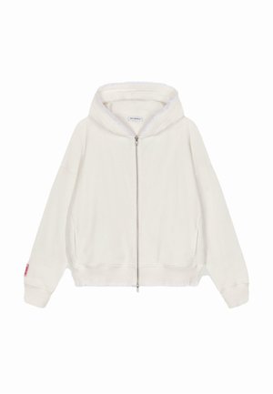 Veste à zip blanche en tissu doux, avec des manches larges, des poignets et un ourlet côtelés, et une capuche doublée. Petite étiquette logo sur la manche gauche.