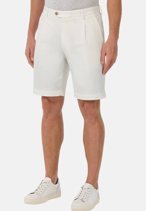 Pantalones cortos blancos ajustados con un frente plano, dos bolsillos laterales y un cierre de un solo botón, combinados con zapatillas blancas.