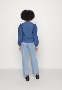 Camicia in denim con dettagli di spalle arricciate, di colore blu, e maniche a palloncino, abbinata a jeans azzurri chiari e tacchi chunky neri.