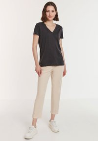 Donkergrijze t-shirt met korte mouwen en V-hals, zachte stof, gecombineerd met lichtbeige slim-fit broek en witte sneakers. Eenvoudig en modern ontwerp.
