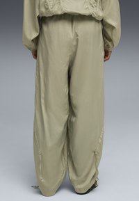 Pantaloni leggeri di colore verde oliva chiaro, dalla vestibilità ampia e con una finitura testurizzata, dotati di tasche laterali e coulisse regolabili ai piedi.