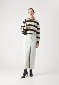 Randig brun och gräddfärgad tröja, högmidjade ljusblå denimkjol med en framslits, svarta ankelboots och en liten svart handväska.