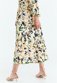 Rochie maxi florală cu un model multicolor de galben, verde și negru pe un fond alb, având talie elastică și mâneci lungi.
