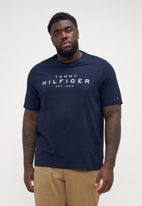 Tumši zilas krāsas t-krekls ar īsām piedurknēm, kas attēlo "TOMMY HILFIGER EST.1985" logo baltā krāsā, apaļa kakla izgriezums un patīkama kokvilnas tekstūra.