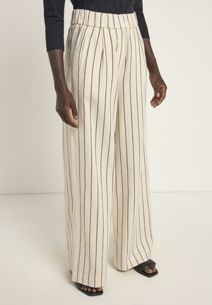 Wide-leg trousers in light beige fabric with vertical navy stripes, featuring a high waistband and front pleats. Black heeled sandals visible.