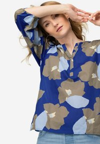 Blusa floreale blu con maniche a tre quarti, presenta fiori azzurri e taupe su uno sfondo blu. Design a scollo a V, vestibilità rilassata.