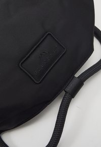 Black fabric bag with textured surface, featuring a raised logo patch and braided strap. Compact design with minimal detailing.
