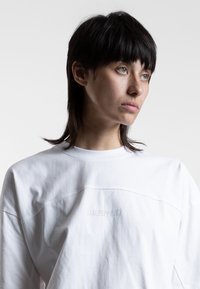 Witte katoenen longsleeve shirt met een ronde hals, voorzien van een subtiele textuur en een vaag logo op de achterkant.