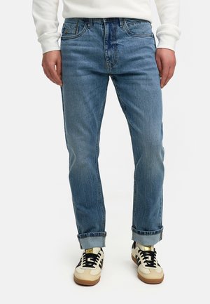 Lyse blå denimjeans med rett passform, synlig falming og rullet opp ermer, kombinert med kremfargede og svarte joggesko.