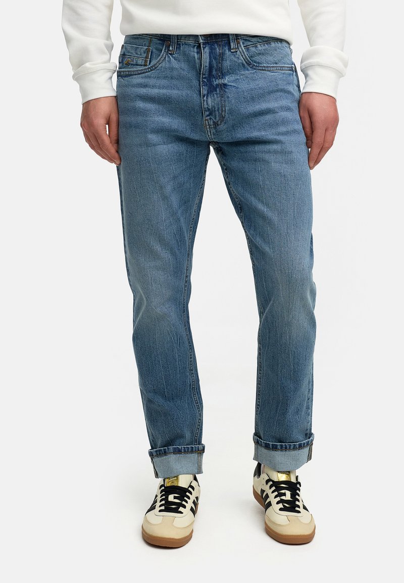 Lyse blå denimjeans med rett passform, synlig falming og rullet opp ermer, kombinert med kremfargede og svarte joggesko.