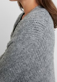 Gray knitted shawl made of soft wool, featuring a textured ribbed pattern and draped over the shoulder, with a loose fit and open front.