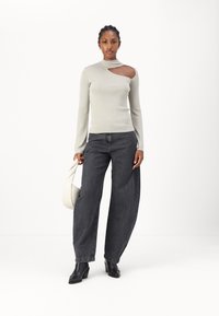 Haut à manches longues gris clair avec un détail découpé et un col montant, associé à un jean large gris foncé et des bottines noires à talons.