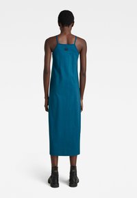 Turkoosi puuvillainen midi-mekko ohutolkaimilla, suora leikkaus ja LOGO-tunniste takana, yhdistettynä mustiin nauhakengiin.