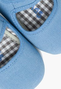 Jasnoniebieskie płócienne buty o zaokrąglonym kształcie, z szaro-białą w kratkę podszewką i wyciętymi otworami po bokach.