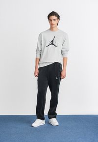 Grauer Sweatshirt mit schwarzem Jordan-Logo, kombiniert mit schwarzen Jogginghosen mit hellblauen Seitenstreifen und weißen Turnschuhen.