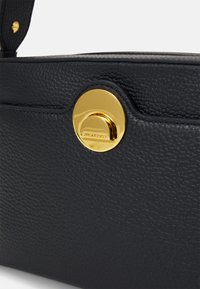 Schwarze strukturierten Lederhandtasche mit einem goldenen, runden Verschlussdetail. Hat ein schlankes, kompaktes Design.