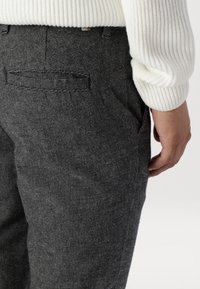 Tailored dark gray trousers with a houndstooth pattern, featuring a textured fabric, side pockets, and a back pocket.