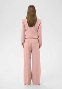 Rosa maßgeschneiderter Anzug mit strukturiertem Blazer und weitem Hose. Glattes Gewebe, dezente Textur und drei Knopfakzente an den Ärmel.