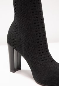 Czarne botki na wysokim obcasie z teksturowanej dzianiny, z pionowymi wycięciami, okrągłym noskiem i gładkim, jednolitym obcasem.