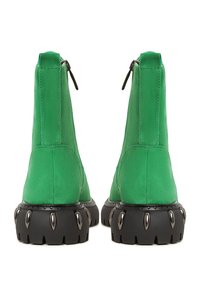 Botas de tobillo de ante verde con cremallera en la parte trasera, suela negra gruesa con acentos salientes y un acabado suave y texturizado.