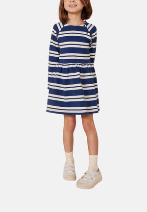 Blau-weiß gestreiftes Kleid mit langen Ärmeln, gerafftem Taillenbund und rundem Ausschnitt. Getragen mit weißen Klettschuhen und knielangen Socken.