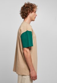 Beige póló zöld rövid ujjal, pamutból készült. Lazább szabással és egyszerű dizájnnal rendelkezik, kontrasztos színekkel.