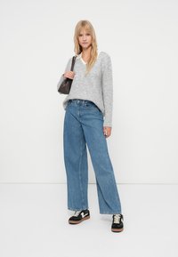 Gaiši pelēks faktūrēts džemperis ar V veida kaklu, augstām vidukļa zilām platajām biksēm, melni sporta apavi ar baltām akcentiem un neliela tumša plecu soma.