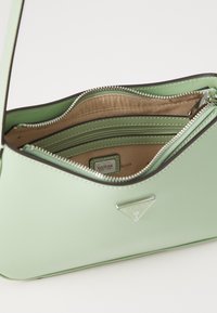 Sac à main en simili cuir vert, avec une forme structurée, des ferrures en argent et plusieurs compartiments zippés. L'intérieur est doublé de beige.