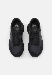 Schwarze Sportschuhe aus einer Mischung von Stoff und Wildleder, ausgestattet mit strukturierten Einsätzen, Schnürsenkeln und einer gepolsterten Sohle, die für Komfort und Unterstützung sorgen.